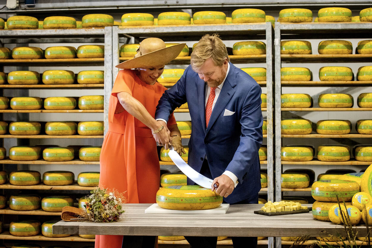 Koning en Koningin snijden samen een kaas met een kaasmes.