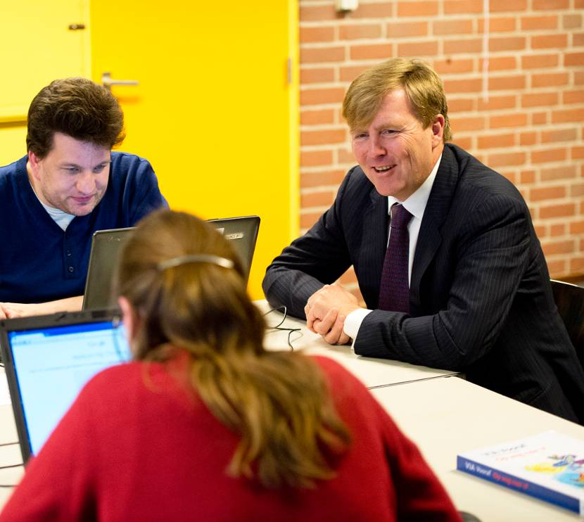 De Koning is in gesprek met 2 cursisten die computeronderwijs volgen bij avondschool Prago.