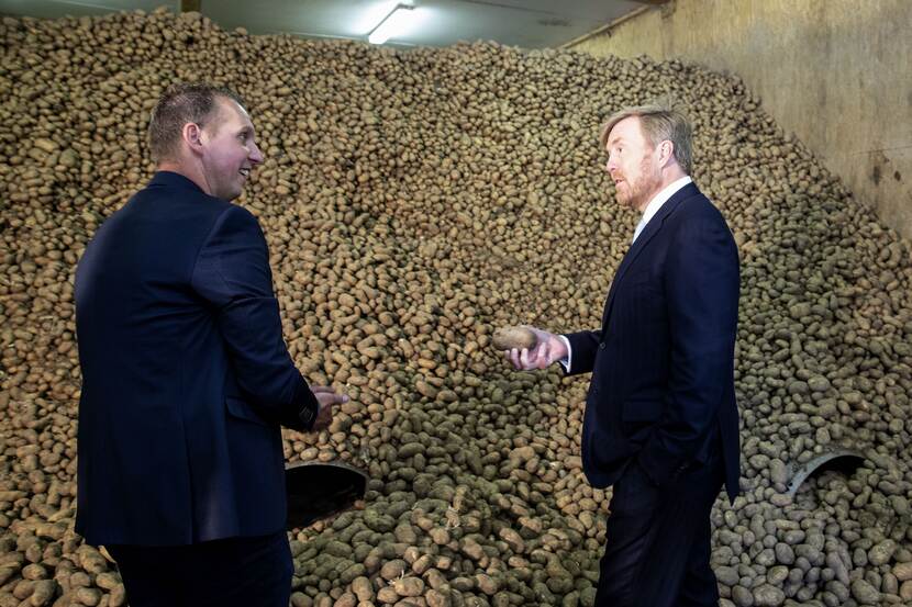 Koning Willem-Alexander in gesprek met een agrariër, staand voor een grote voorraad aardappelen