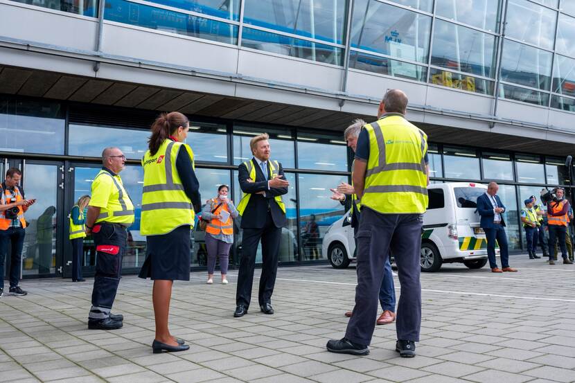Koning Willem-Alexander voor de ingang van Schiphol in gesprek met luchthavenpersoneel