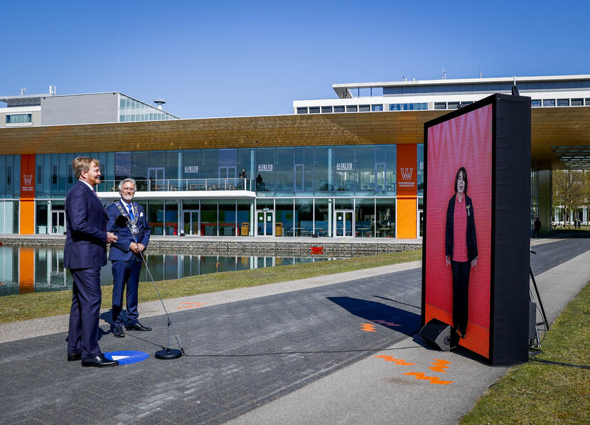 Koning Willem-Alexander, met naast zich de Eindhovense burgemeester, staat voor een videoscherm.