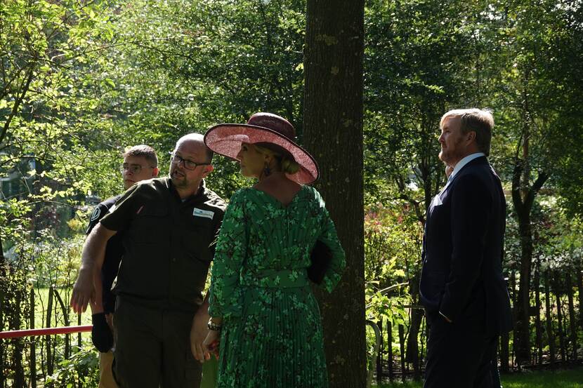 Het Koningspaar in gesprek in een groene omgeving.
