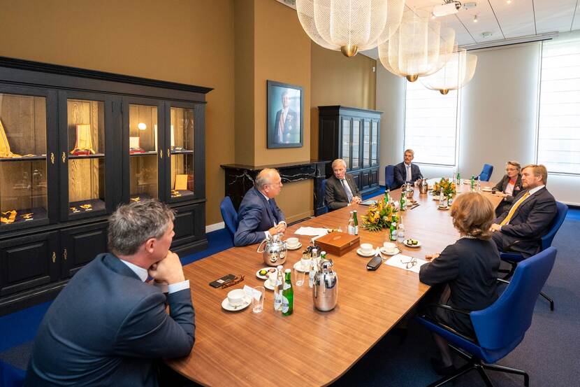 Koning Willem-Alexander in gesprek aan tafel met anderen.