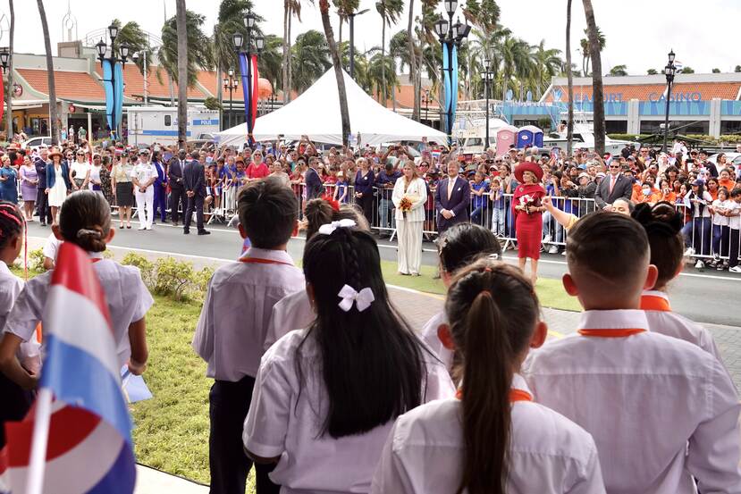 Koning Willem-Alexander, Koningin Máxima en de Prinses van Oranje luisteren naar zingende kinderen op Aruba